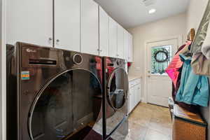 Laundry room featuring light tile patterned flooring, washer and dryer, and cabinets