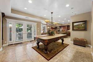 Game room with a textured ceiling, a chandelier, french doors, and light tile patterned floors