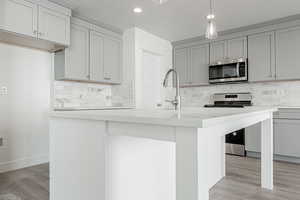 Kitchen featuring decorative backsplash, a kitchen island with sink, gray cabinets, and appliances with stainless steel finishes