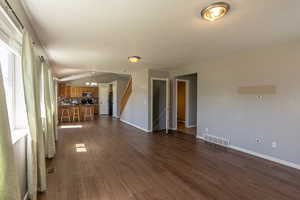 Unfurnished living room featuring dark hardwood / wood-style floors, vaulted ceiling, sink, and a chandelier