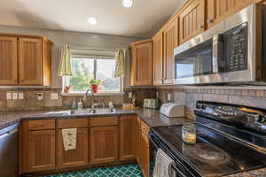 Kitchen with sink, appliances with stainless steel finishes, tile patterned flooring, and backsplash