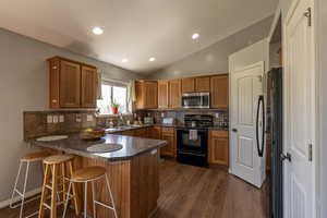 Kitchen featuring tasteful backsplash, kitchen peninsula, dark wood-type flooring, black range with electric stovetop, and vaulted ceiling