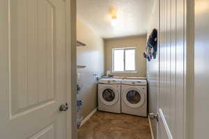 Laundry room with dark tile patterned floors, washing machine and dryer, and a textured ceiling