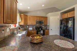 Kitchen with decorative backsplash, black appliances, sink, and vaulted ceiling