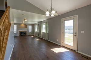 Unfurnished living room with a fireplace, dark hardwood / wood-style floors, lofted ceiling, and a notable chandelier