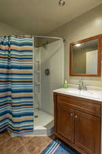 Bathroom featuring walk in shower, tile patterned floors, vanity, and a textured ceiling