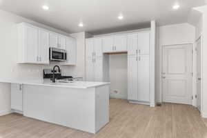 Kitchen with light hardwood / wood-style floors, white cabinetry, kitchen peninsula, and gas stove