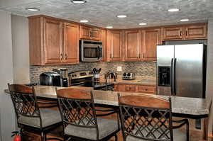 Kitchen featuring decorative backsplash, appliances with stainless steel finishes, a textured ceiling, and a breakfast bar