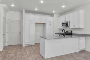 Kitchen with white cabinets, stainless steel appliances, light hardwood / wood-style flooring, and kitchen peninsula