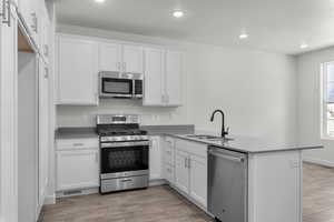 Kitchen featuring appliances with stainless steel finishes, white cabinets, hardwood / wood-style floors, sink, and kitchen peninsula