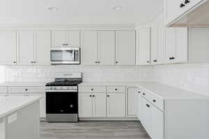 Kitchen with tasteful backsplash, appliances with stainless steel finishes, light hardwood / wood-style flooring, and white cabinets