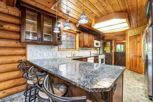 Kitchen with tasteful backsplash, white appliances, wood ceiling, pendant lighting, granite countertops, and rustic walls