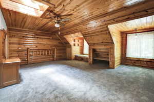 Primary bedroom with carpet, rustic walls, lofted ceiling with skylight, wooden ceiling, and ceiling fan