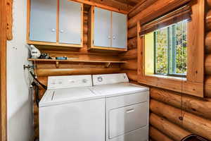 Clothes washing area with log walls, independent washer and dryer, cabinets, and a wealth of natural light