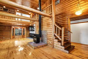 Unfurnished living room featuring a wood stove, wood ceiling, log walls, hardwood / wood-style floors, and a towering ceiling