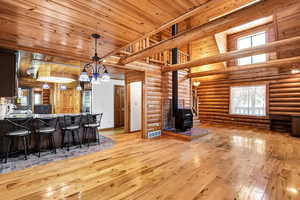 Interior space featuring a wood stove, kitchen peninsula, log walls, light hardwood / wood-style floors, and hanging light fixtures