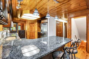 Kitchen with wooden walls, hanging light fixtures, light hardwood / wood-style floors, and stainless steel fridge with ice dispenser