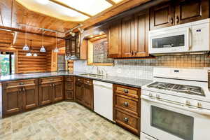 Kitchen with dark granite counters, white appliances, sink, decorative light fixtures, and rustic walls