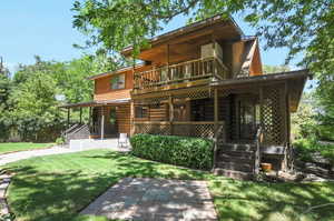 View of back of home with a balcony and a yard