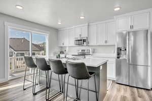 Kitchen featuring appliances with stainless steel finishes, light hardwood / wood-style flooring, white cabinets, and an island with sink