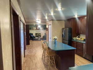 Kitchen with stainless steel fridge with ice dispenser, crown molding, a center island, light hardwood / wood-style flooring, and a kitchen breakfast bar