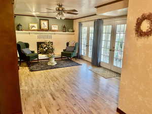 Living area featuring wood-type flooring, french doors, fireplace, ornamental molding, and ceiling fan