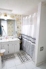 Bathroom with double vanity, a textured ceiling, and tile patterned floors