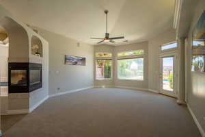 Unfurnished living room with carpet floors, a multi sided fireplace, ceiling fan, and vaulted ceiling