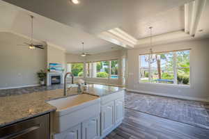 Kitchen featuring white cabinets, ceiling fan with notable chandelier, wood-type flooring, and pendant lighting