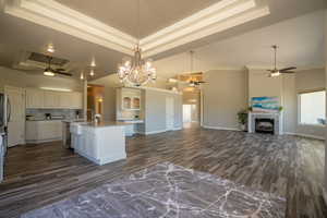 Kitchen featuring a kitchen island with sink, ceiling fan with notable chandelier, and a tray ceiling