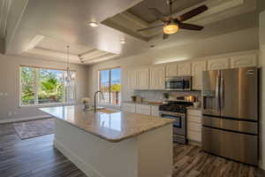 Kitchen with a raised ceiling, appliances with stainless steel finishes, a center island with sink, and plenty of natural light