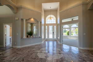 Tiled entrance foyer featuring a high ceiling, ornate columns, and a notable chandelier