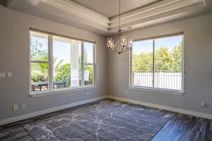 Spare room with an inviting chandelier, dark wood-type flooring, and a raised ceiling