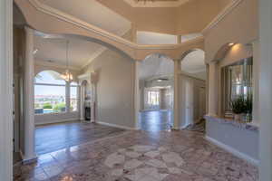 Foyer with tile patterned floors, a high ceiling, ceiling fan with notable chandelier, ornamental molding, and decorative columns