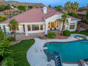 Back house at dusk with a patio, a pool with hot tub, and a yard