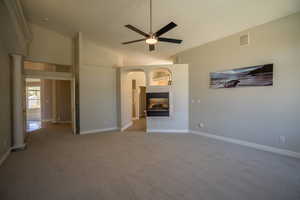 Unfurnished living room featuring ceiling fan, high vaulted ceiling, carpet flooring, a tile fireplace, and a textured ceiling