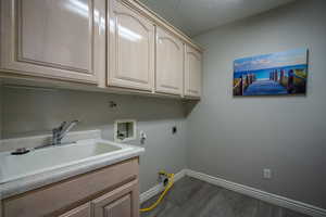 Clothes washing area with hookup for an electric dryer, a textured ceiling, cabinets, washer hookup, and wood-type flooring