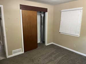 Unfurnished bedroom featuring dark carpet and a closet