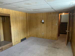 Unfurnished room with wood walls, a paneled ceiling, and carpet