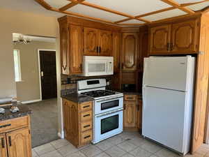 Kitchen featuring dark stone counters, decorative backsplash, white appliances, coffered ceiling, and light tile patterned floors