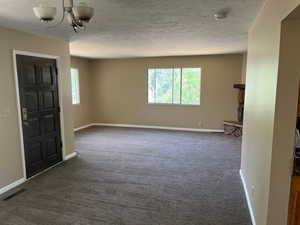 Empty room featuring dark colored carpet, an inviting chandelier, and a textured ceiling