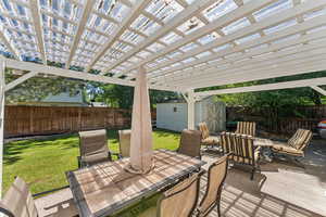 Wooden terrace featuring a pergola, a patio, a yard, and a storage unit