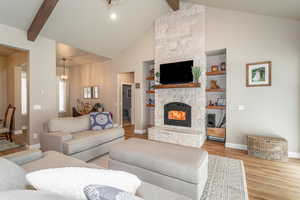 Living room featuring light hardwood / wood-style floors, beamed ceiling, built in shelves, high vaulted ceiling, and a stone fireplace