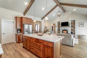 Kitchen featuring light wood-type flooring, hanging light fixtures, a kitchen island, a fireplace, and high end refrigerator