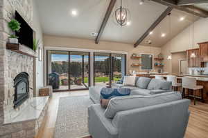 Living room with an inviting chandelier, beamed ceiling, light hardwood / wood-style flooring, and a fireplace