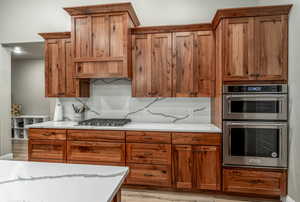 Kitchen with decorative backsplash, light hardwood / wood-style floors, light stone countertops, and stainless steel appliances