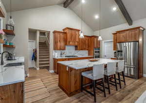 Kitchen featuring beam ceiling, decorative light fixtures, stainless steel appliances, light wood-type flooring, and a kitchen bar