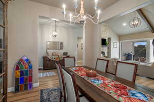 Dining space featuring vaulted ceiling with beams, an inviting chandelier, light hardwood / wood-style flooring, and a fireplace