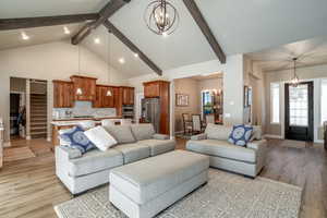 Living room featuring light wood-type flooring, beam ceiling, a chandelier, and high vaulted ceiling