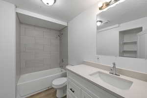 Full bathroom featuring vanity, tiled shower / bath, hardwood / wood-style floors, toilet, and a textured ceiling